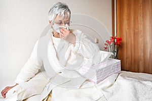 Coronavirus pandemic. Healthcare, flu, hygiene and people concept. Sick senior woman with paper wipe blowing his nose at