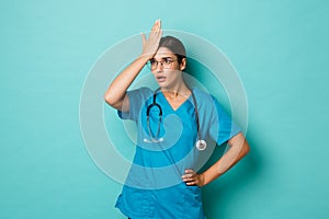 Coronavirus, pandemic and social distancing concept. Image of annoyed female doctor in scrubs and glasses, facepalm and