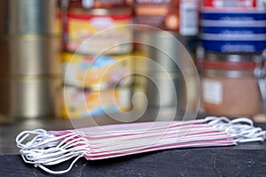 Coronavirus panic concept. Focus on stack of surgical masks on table over a pile of canned foods with a long shelf life such as
