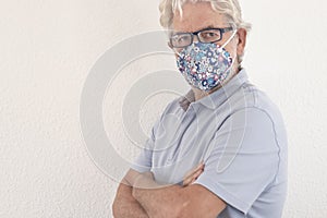 Coronavirus. Portrait of serious senior man wearing protective face mask due to coronavirus looking at camera with crossed arms