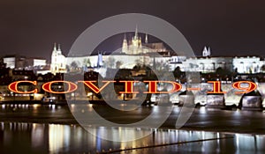 Coronavirus in Prague, Czech Republic. Vltava river, Charles Bridge and St. Vitus Cathedral. Covid-19 sign on a blurred background