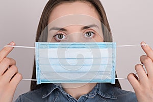Coronavirus protection concept. Close up photo of young woman wearing blue medical mask on face isolated on grey background