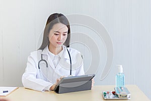 Serious professional doctor wearing white coat and stethoscope holding modern touchscreen gadget