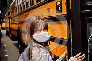 Coronavirus reopening school: wearing face mask. Girl with facemask boarding a school bus