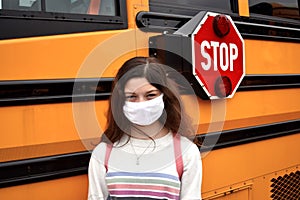 Coronavirus school reopening concept: girl with face mask by school bus photo