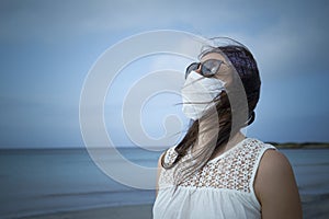 Coronavirus seaside holidays: half-length shot of a woman at the beach looking at the sun with the mask for Covid-19 pandemic