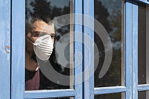 Coronavirus. Sick man of corona virus  looking through the window and wearing mask protection and recovery from the illness in hom photo