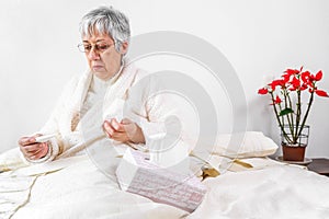 Coronavirus. Sick senior woman holding tissue and thermometer sit on bed, upset old mature woman caught cold got