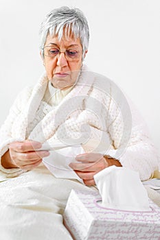 Coronavirus. Sick senior woman holding tissue and thermometer sit on bed, upset old mature woman caught cold got