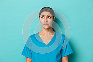 Coronavirus, social distancing and health concept. Close-up of nervous female doctor in scrubs, biting lip and frowning