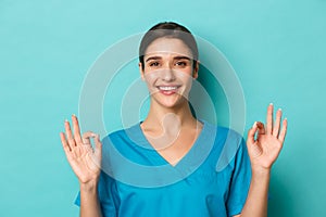 Coronavirus, social distancing and health concept. Close-up of smiling female doctor in scrubs, showing okay sign in