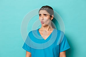 Coronavirus, social distancing and health concept. Close-up of worried brunette female doctor in scrubs, grimacing and