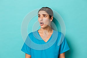 Coronavirus, social distancing and health concept. Close-up of worried young female doctor in scrubs, frowning and