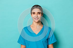 Coronavirus, social distancing and health concept. Close-up of young smiling female doctor, wearing scrubs, looking