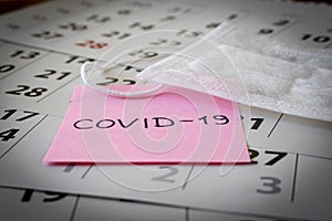 CORONAVIRUS. A sticker with the inscription COVID-19 and a protective medical mask on the calendar sheets. The concept of