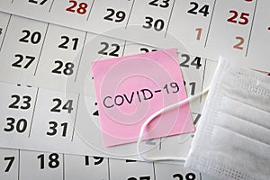 CORONAVIRUS. A sticker with the inscription COVID-19 and a protective medical mask on the calendar sheets. The concept of