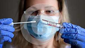 Coronavirus swab collection kit in doctor hands, woman in medical mask holds tube of COVID-19 PCR test