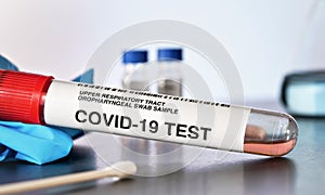 Coronavirus test concept - vial sample tube with cotton swab, blue gloves near, blurred lab glass background, closeup detail.