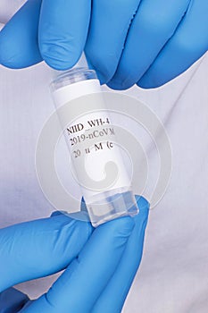 Coronavirus test sample or Covid-19 vial held between the blue gloved hands of a lab technician