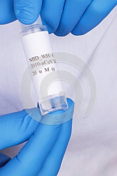 Coronavirus test sample or Covid-19 vial held between the blue gloved hands of a lab technician