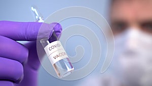 Coronavirus vaccine ampoule in doctor`s hands in face mask and protective medical gloves on a blue background