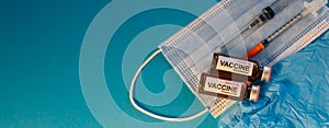 Coronavirus vaccine in bottles on blue background with copy space. Vials of medicine for covid19, syringe, medical face mask and