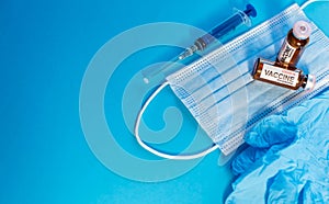 Coronavirus vaccine in bottles on blue background with copy space. Vials of medicine for covid19, syringe, medical face mask and