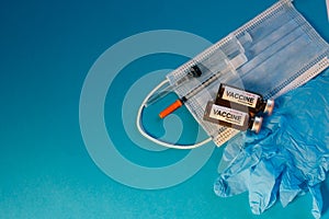 Coronavirus vaccine in bottles on blue background with copy space. Vials of medicine for covid19, syringe, medical face mask and