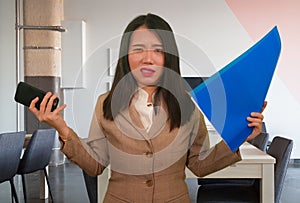 Corporate business stress portrait of young attractive upset and stressed executive Asian Chinese woman tired and unhappy holding