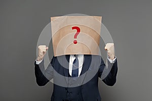 Corporate businessman hiding under paper bag with question mark on grey background