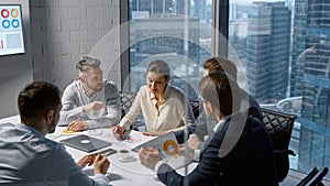 Corporate businesswoman communicating with team while sitting at desk in meeting room