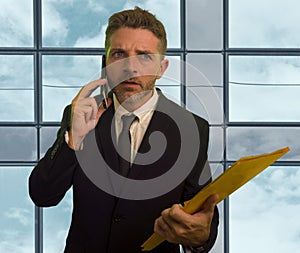 Corporate company work lifestyle portrait of stressed and frustrated businessman talking on mobile phone holding paperwork reports