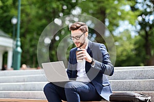 Corporate executive in formal wear sitting on stairs in park with laptop and coffee during lunch break