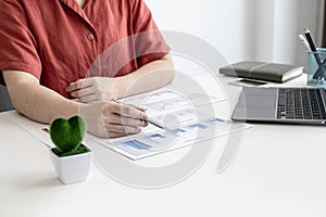 A corporate finance employee is pointing at the document with a pen to verify the accuracy of the financial documents.
