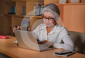 Corporate job lifestyle portrait of happy and successful attractive middle aged Asian woman working at office laptop computer desk