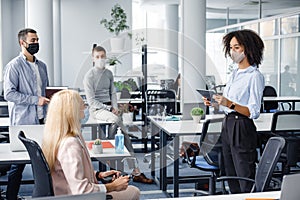 Corporate meeting and group work in company. African american woman manager in protective mask holding tablet, talking