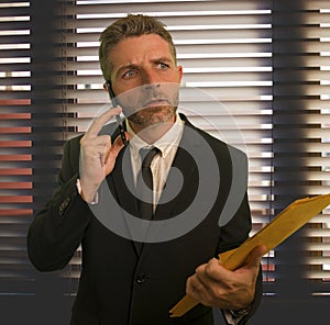 Corporate office lifestyle portrait of serious and worried business man holding paperwork reports talking on mobile phone at