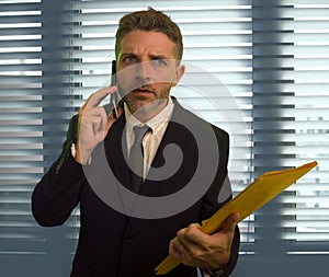 Corporate office lifestyle portrait of serious and worried business man holding paperwork reports talking on mobile phone at