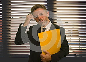 Corporate office lifestyle portrait of stressed and frustrated business man holding paperwork reports overwhelmed and upset at