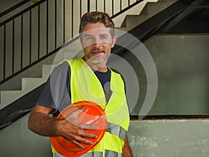 Corporate portrait of young attractive and happy builder man or constructor posing confident smiling wearing building helmet and