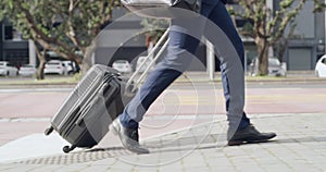 Corporate traveling businessman walking and carrying a suitcase in street of urban city town on his way to the airport