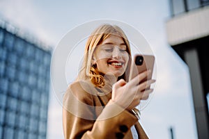 Corporate woman recording audio message while smiling and crossing from office building