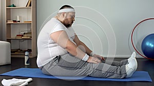 Corpulent man sitting on mat for exercising, labored breathing, obesity problems