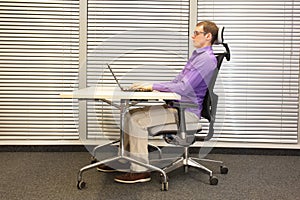 Correct sitting position at workstation. man on chair working with laptop
