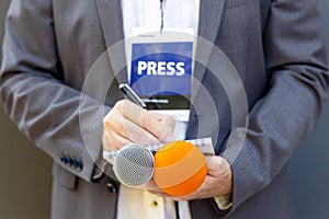 Correspondent or journalist at media event, holding microphone, writing notes. Journalism concept.