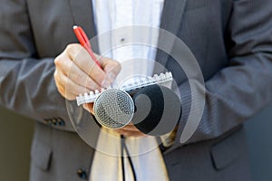 Correspondent or reporter at media event, holding microphone, writing notes. Journalism concept