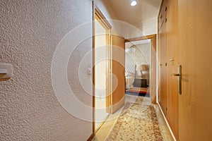 Corridor of a house with white painted walls with gotelet, classic furniture, long carpet on the floor and built-in cabinets on