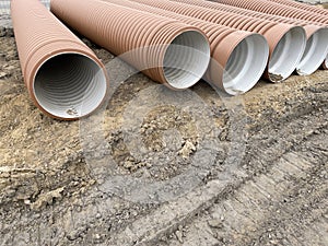 Corrugated Double-Walled Polypropylene Pipes Lined Up at a Construction Site During Daytime. Several large red