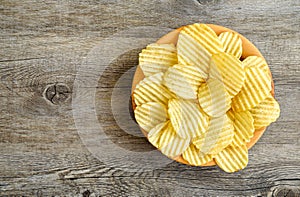 Corrugated golden potato chips in a wooden bowl on rustic wooden table.