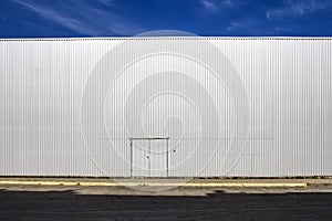 Corrugated sheet metal wall with a door, the street shadows and blue sky. Outdoor. Industrial look. Digital background